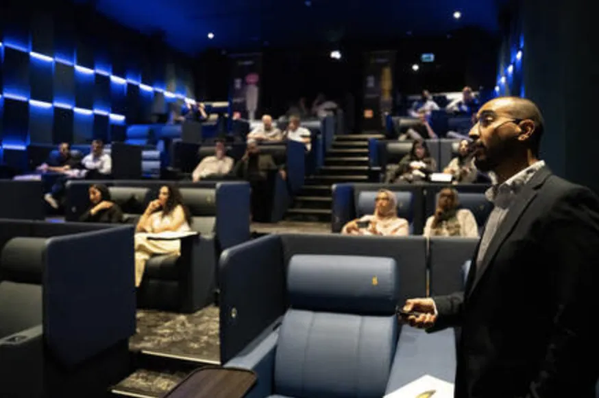 Speaker presenting in a blue-lit cinema